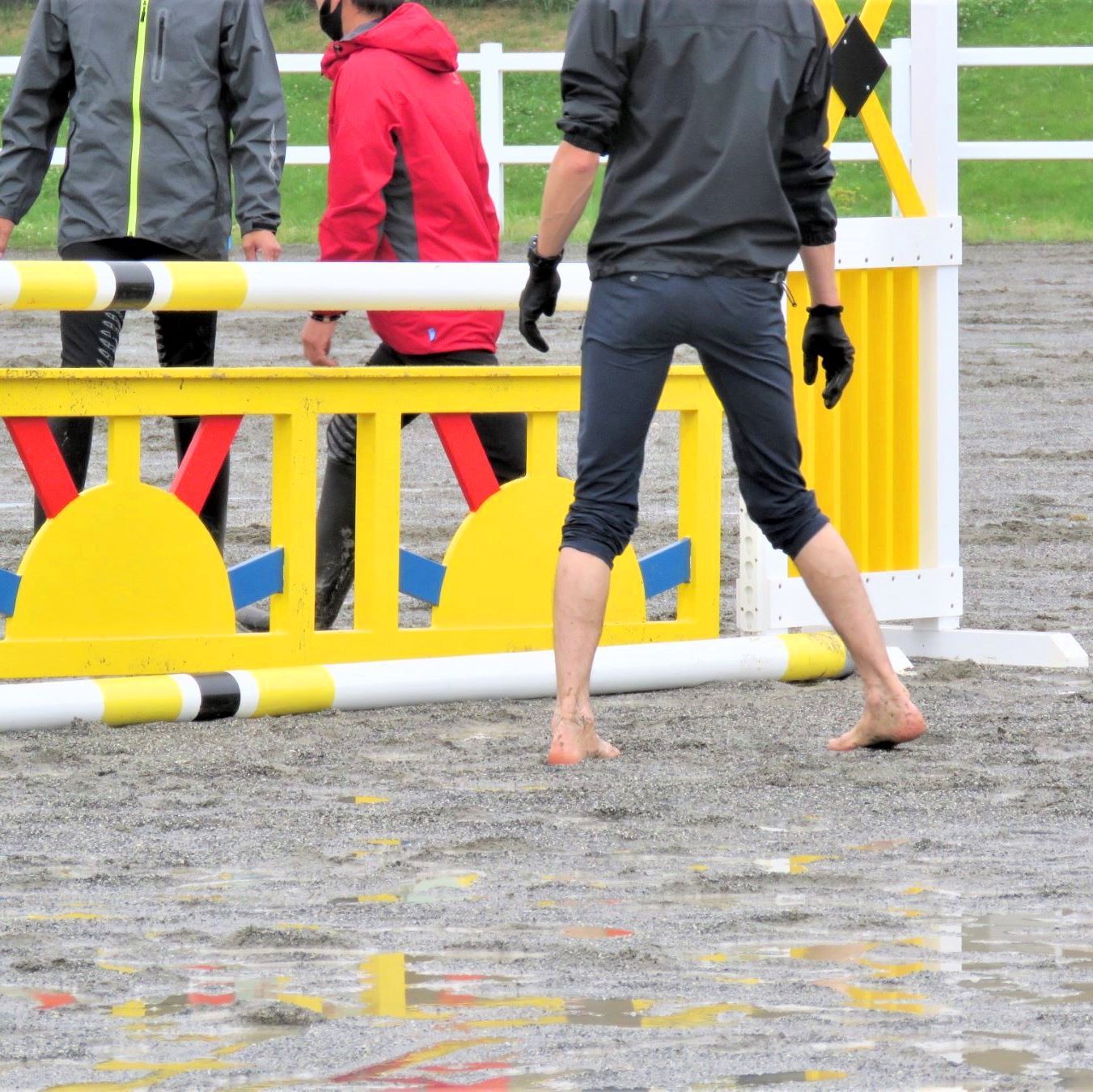 雨でぬかるみのある馬場、裸足で障害の設置を確かめるスタッフ