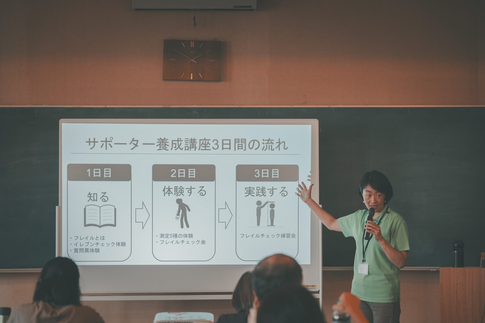 スクリーンに映した「サポーター養成講座3日間の流れ」の資料を示しながら、講座全体の進み方を説明する場面