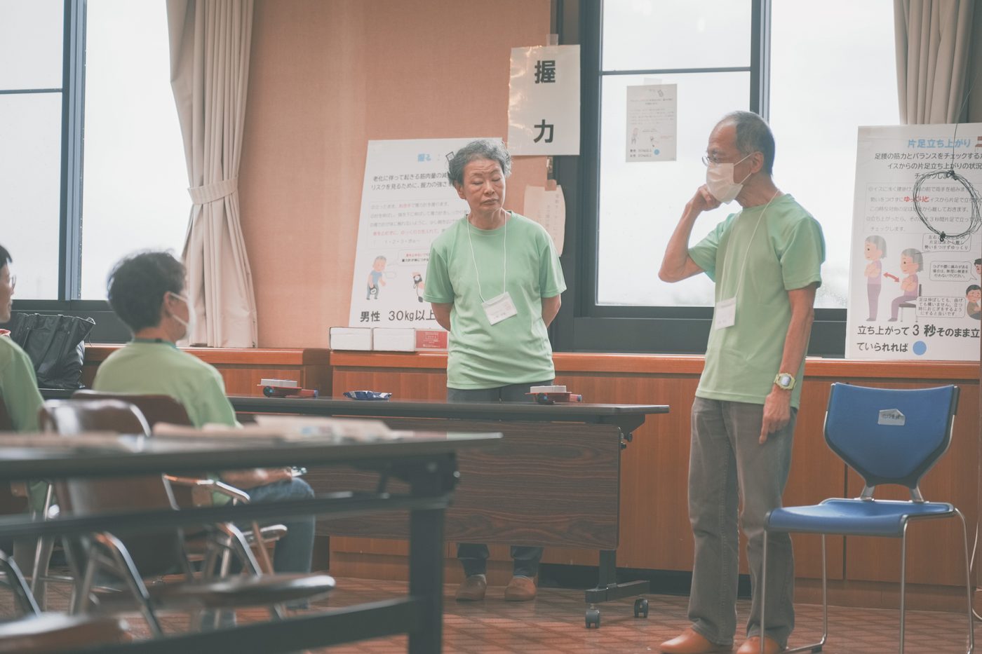 「握力」と掲示された測定ブースで、測定する人と測定を受ける人が向き合い、手順を確認する様子
